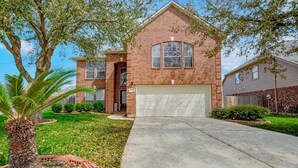 A two-story brick house with a garage, surrounded by a well-maintained lawn and a palm tree.