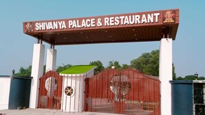 Der Eingang zum Shivanya Palace & Restaurant mit einer großen Schautafel, einem schmiedeeisernen Tor und einem grünen Dach.