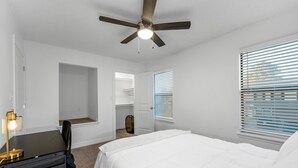 Un dormitorio con cama, escritorio, silla, ventilador de techo y ventana con persianas.