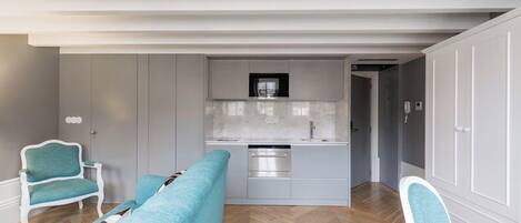 A modern kitchen with white cabinets and stainless steel appliances, a glass-top dining table, and teal chairs.