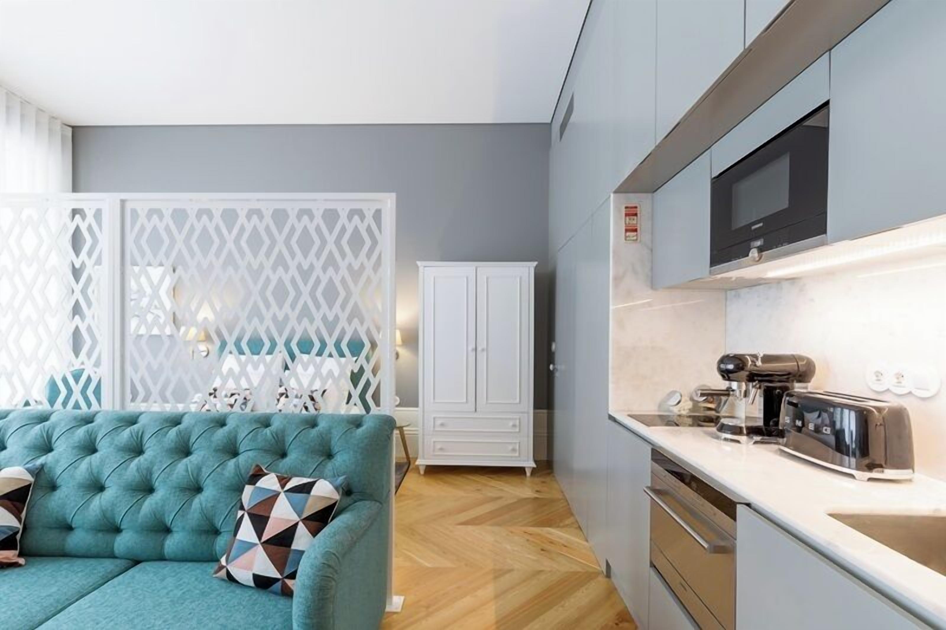 A modern kitchen with a built-in microwave, toaster, and coffee machine. There is a white cabinet and a white partition with geometric patterns.