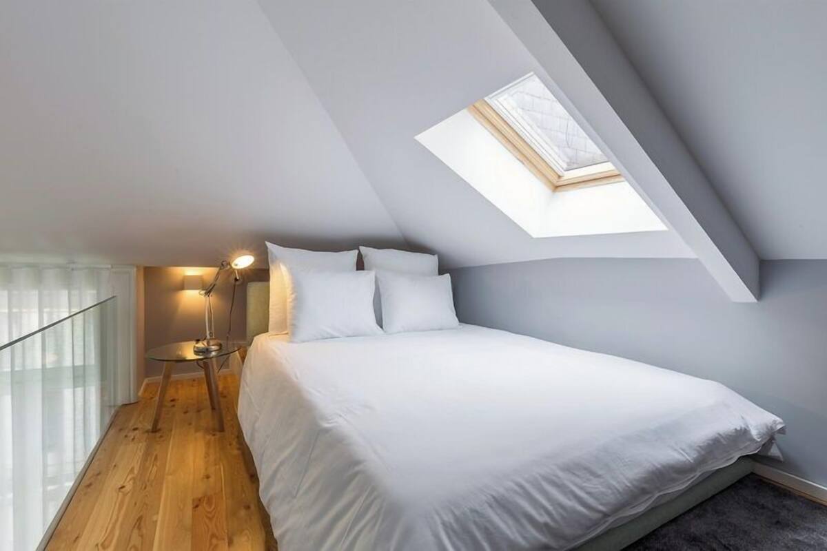 A bedroom with a skylight, a bed, a bedside table, and a lamp.