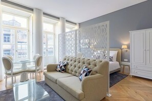 Un dormitorio moderno con un ventanal grande, un sofá capitonado, una mesa de centro de cristal y un armario blanco.