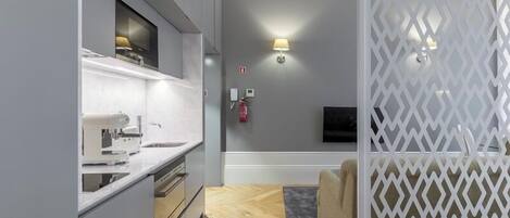 A modern kitchen with a built-in oven, a microwave, and a sink. There is a white partition with a geometric pattern, a wall-mounted TV, and a wall-mounted light fixture.