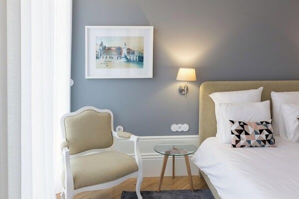 Habitación de hotel con cama, una silla, una mesita y una lámpara de pared.