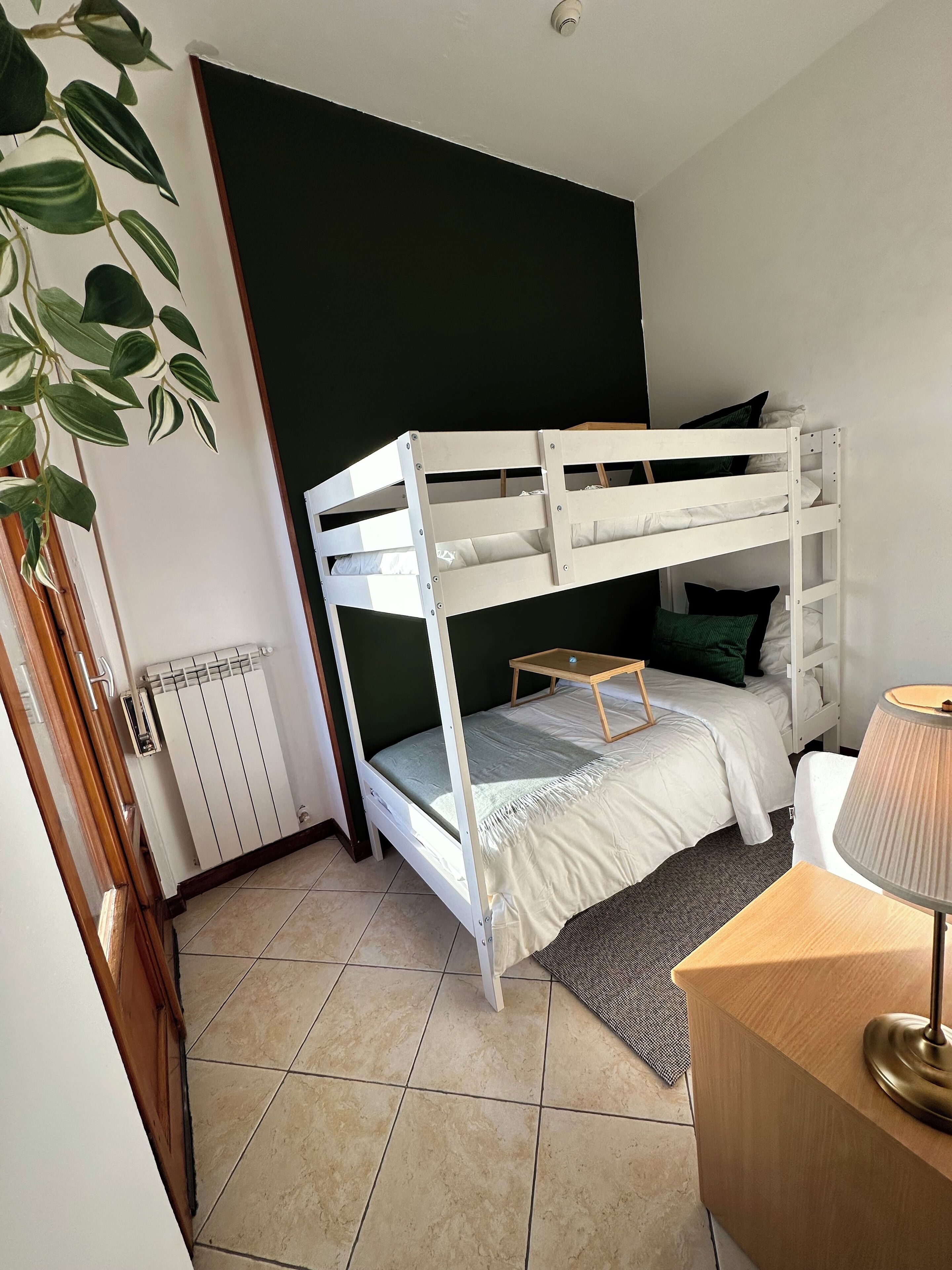 Habitación con literas, un radiador, un escritorio con lámpara y una planta.
