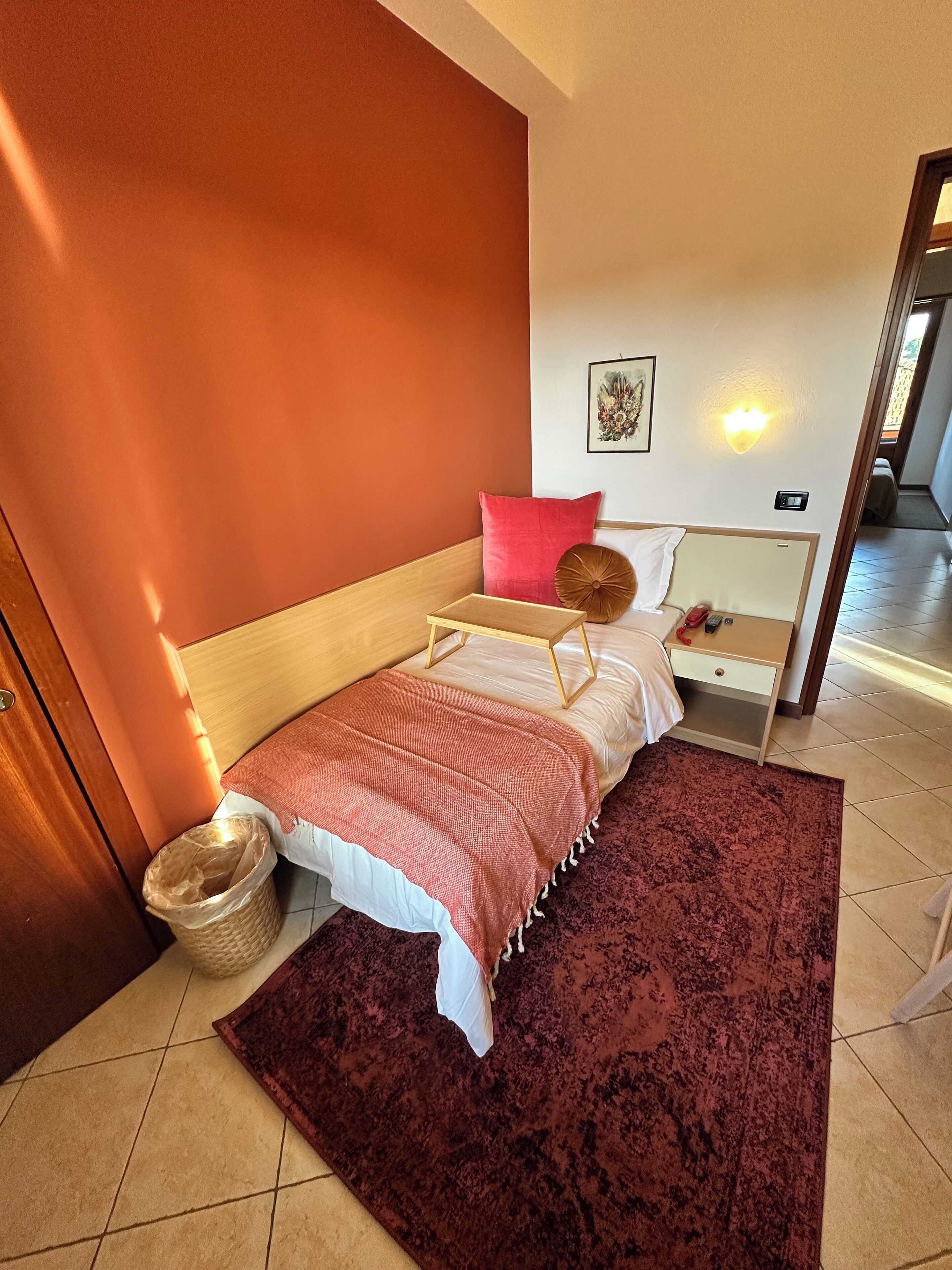 Een slaapkamer met een bed, een nachtkastje, een wandlamp en een deur naar een andere kamer.