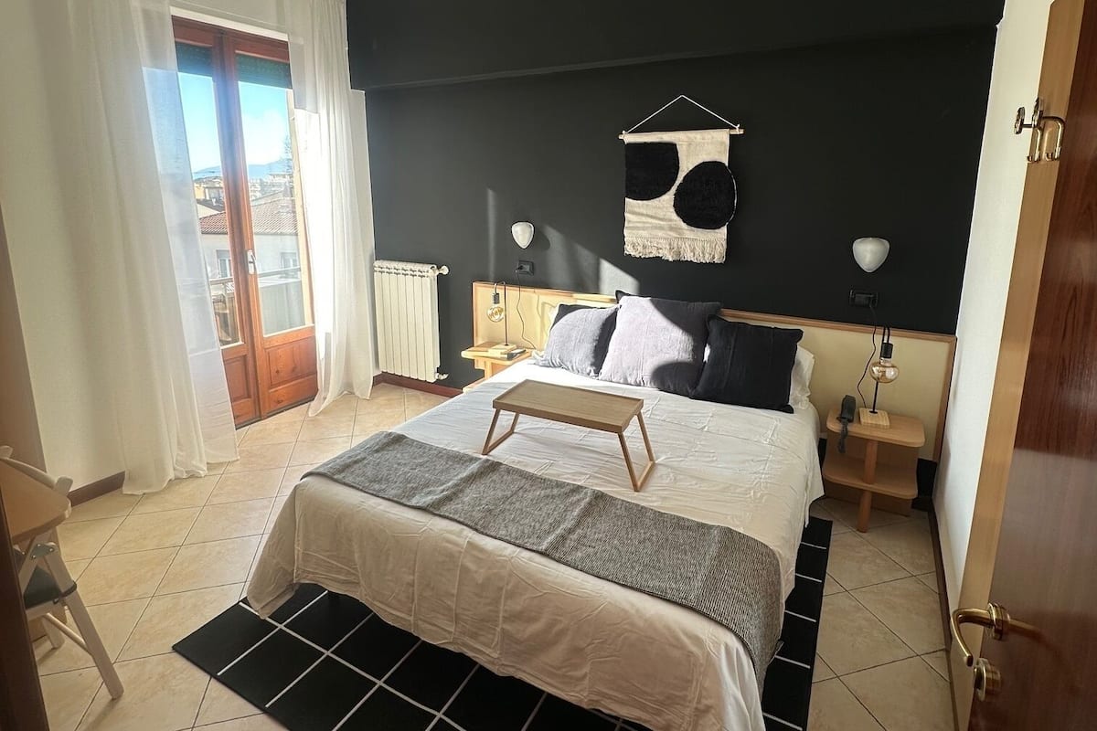Ein Schlafzimmer mit Bett, Nachttischen, einem aufgehängten Handtuch und Blick ins Freie.
