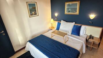 Un dormitorio ordenado con cama, mesitas de noche y lámparas fijadas a la pared.