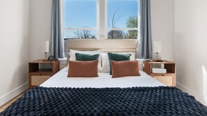 Een slaapkamer met een groot bed, twee nachtkastjes, een raam met gordijnen en uitzicht op bomen.