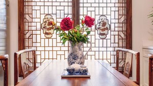 Une table à manger traditionnelle en bois, ornée d’un vase rempli de fleurs rouges et d’une théière posée sur un plateau.