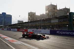 Een Formule 1-auto op een racecircuit met een imposant gebouw op de achtergrond.