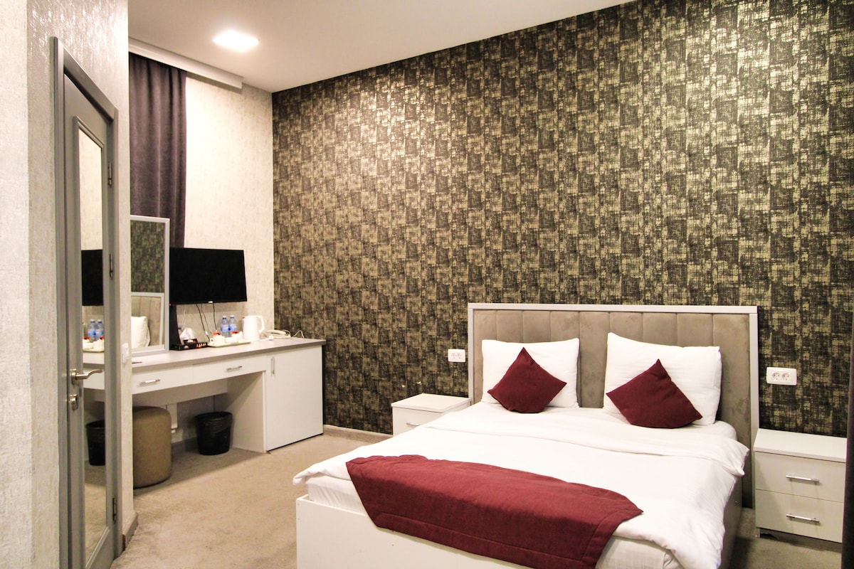 Une chambre d’hôtel avec un lit, un bureau, un miroir et un mur recouvert d’un papier peint à motifs.