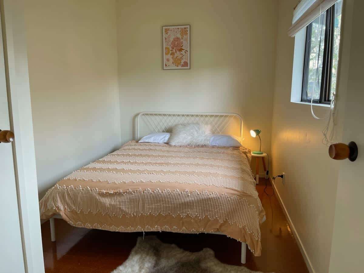 A bedroom with a bed, bedside lamp, and a window with blinds.