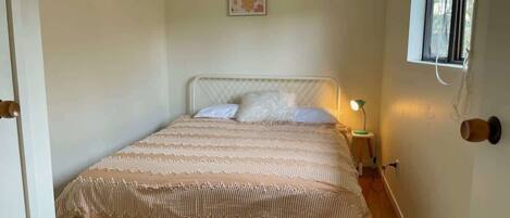 A bedroom with a bed, bedside lamp, and a window with blinds.