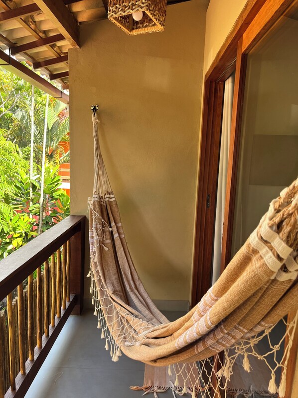 Un hamac sur un balcon doté d’une balustrade en bois, un luminaire suspendu en fibres tressées et une vue sur la verdure environnante.