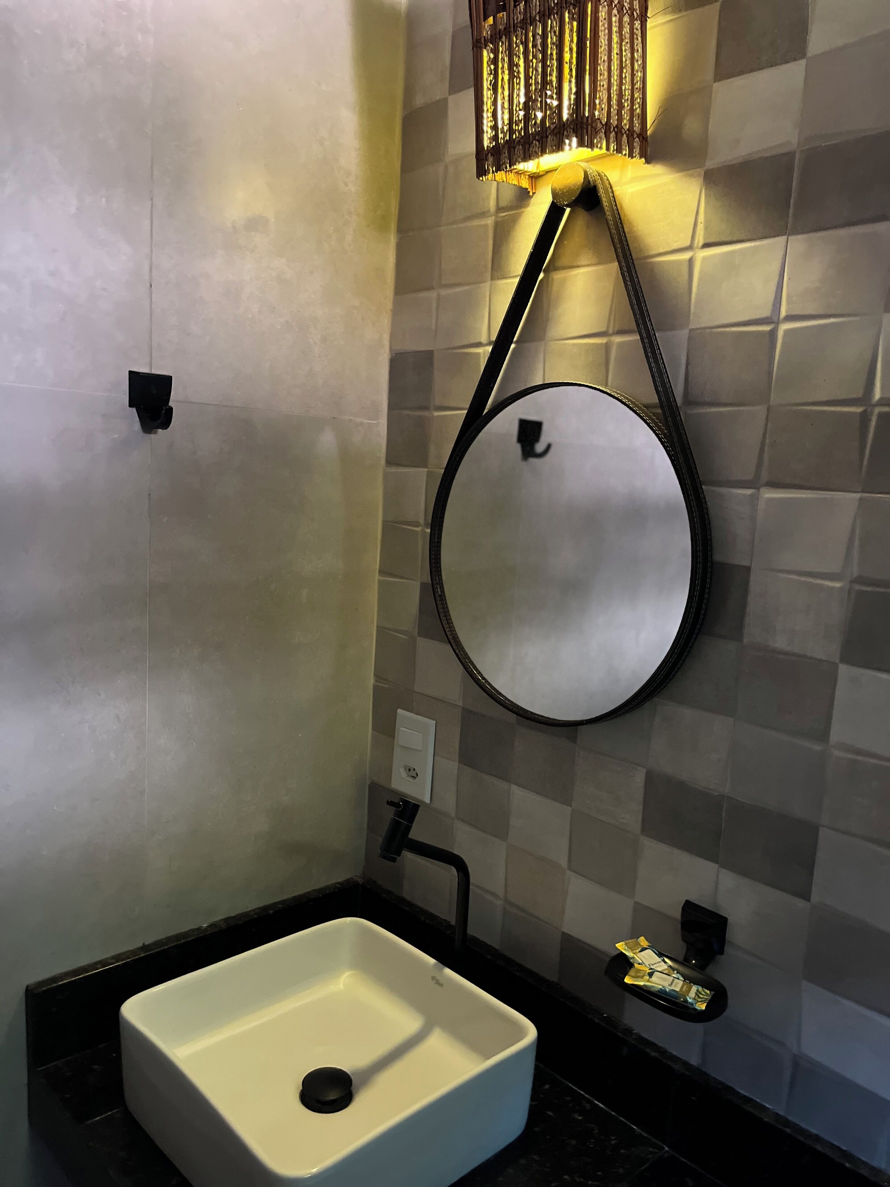 Un baño con un lavamanos blanco, un espejo redondo y una lámpara de pared.