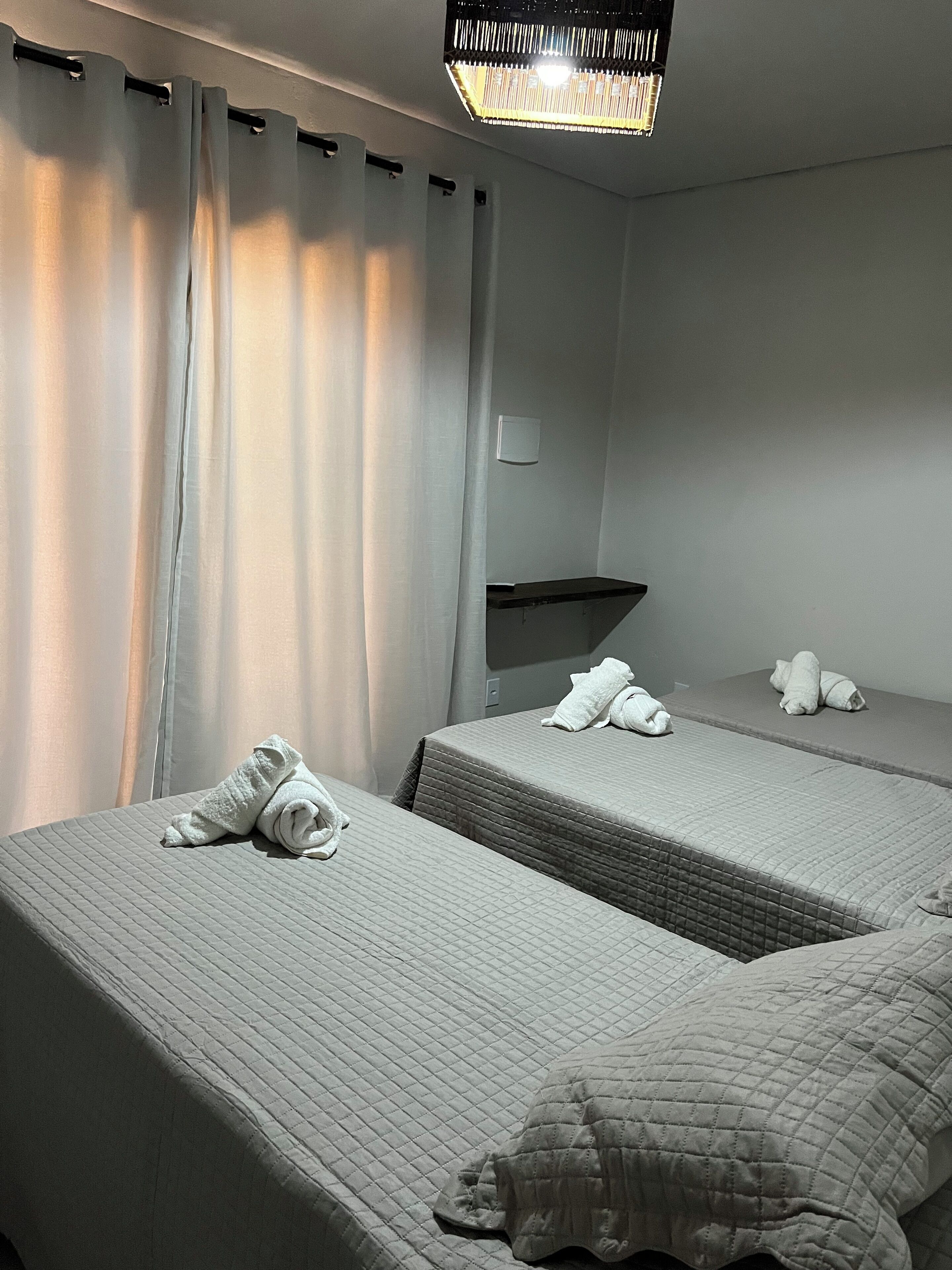 A hotel room with two beds, each with a quilted mattress and pillows, and a small table between them.