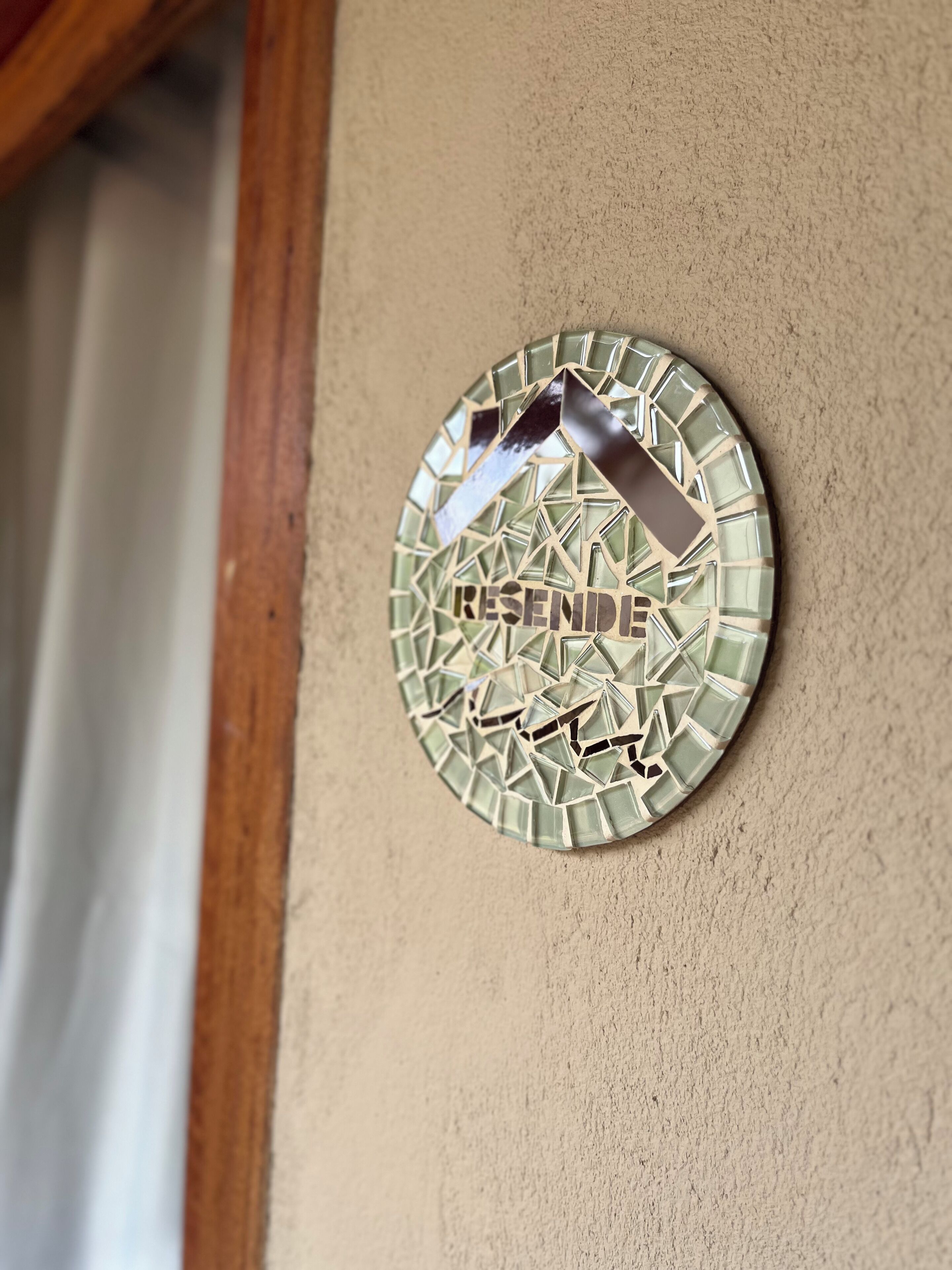 Uma placa circular com padrão de mosaico e a palavra 'RENDRE' em uma parede bege.