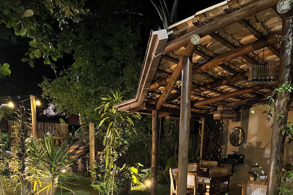 A well-lit outdoor patio area with a pergola, potted plants, and a seating area with tables and chairs.