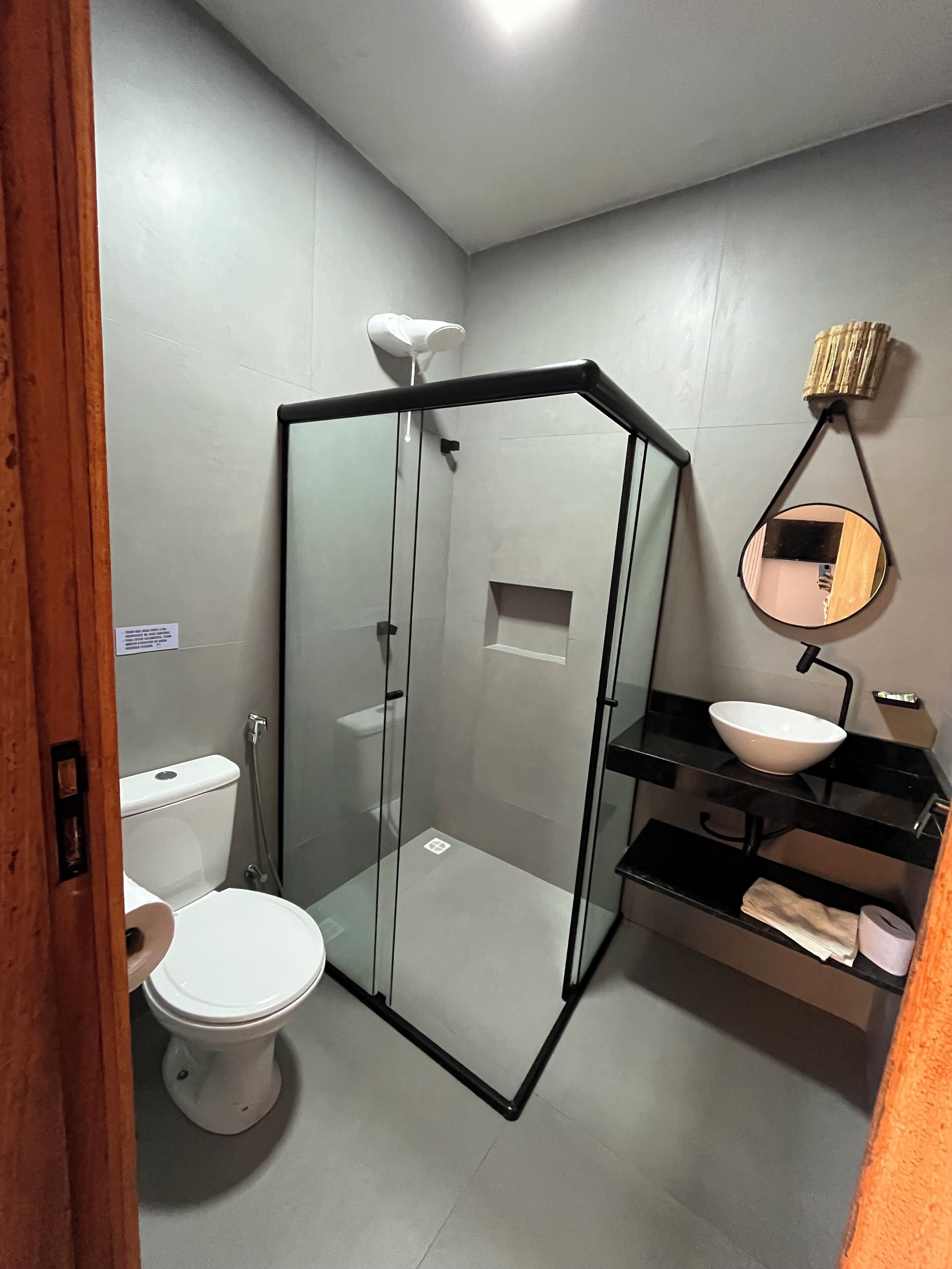 Baño con ducha envuelta en vidrio, inodoro, lavamanos con espejo y toallero.