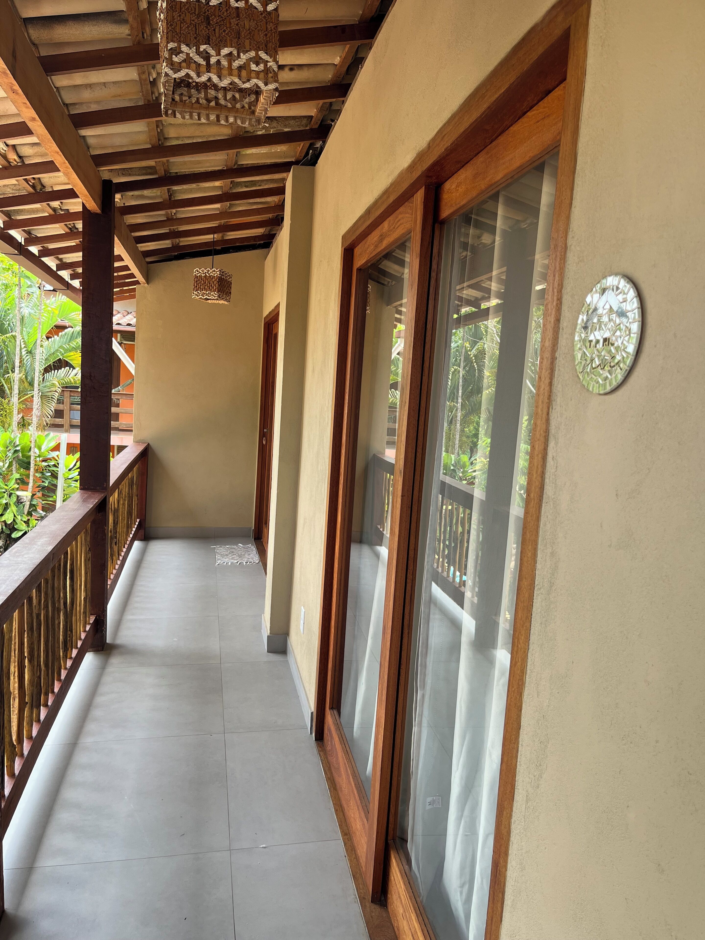 A covered corridor with wooden railings, a tiled floor, and a view of greenery outside.