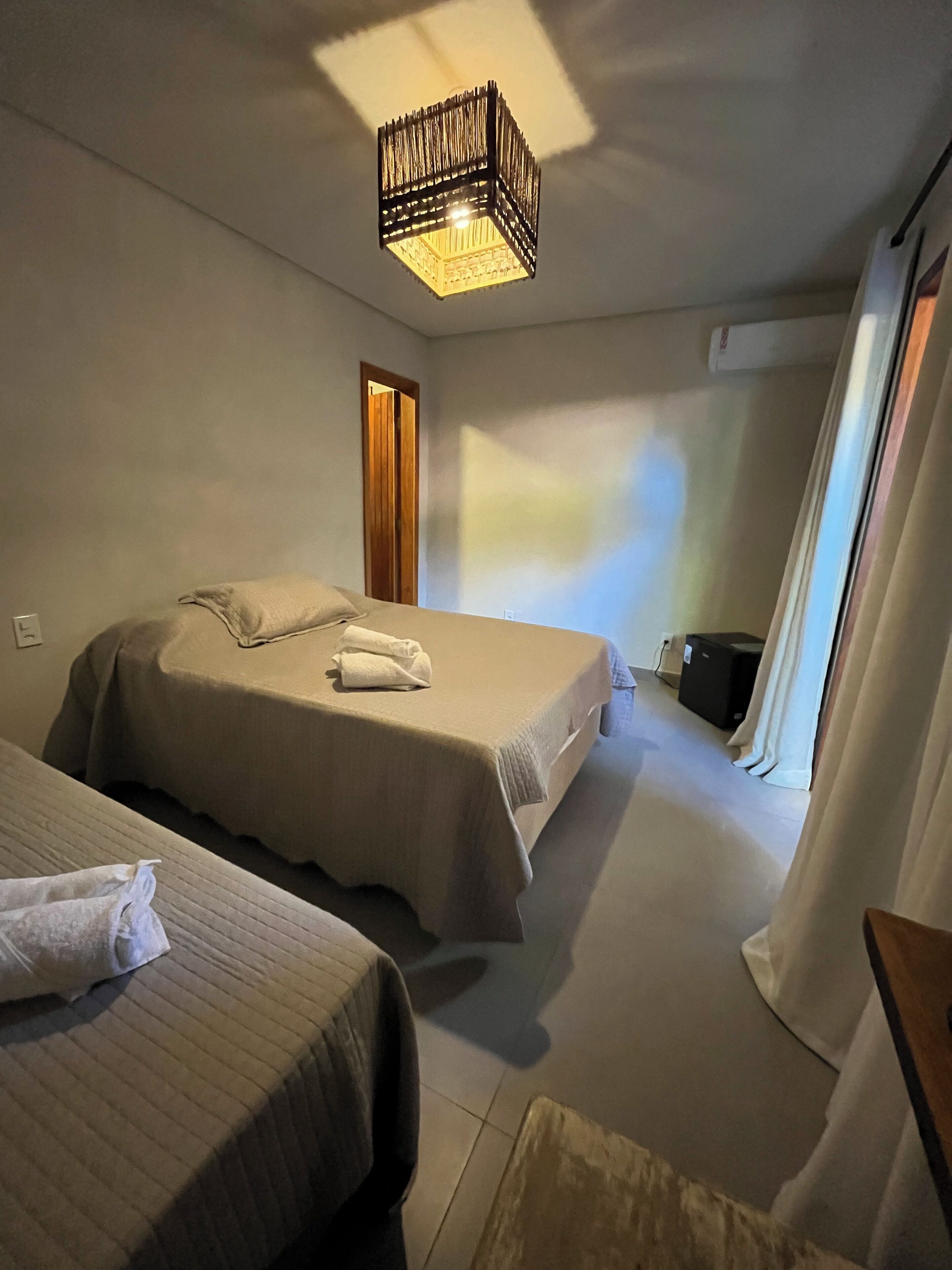 Une chambre d’hôtel avec deux lits, un luminaire au plafond, une porte et une petite table.