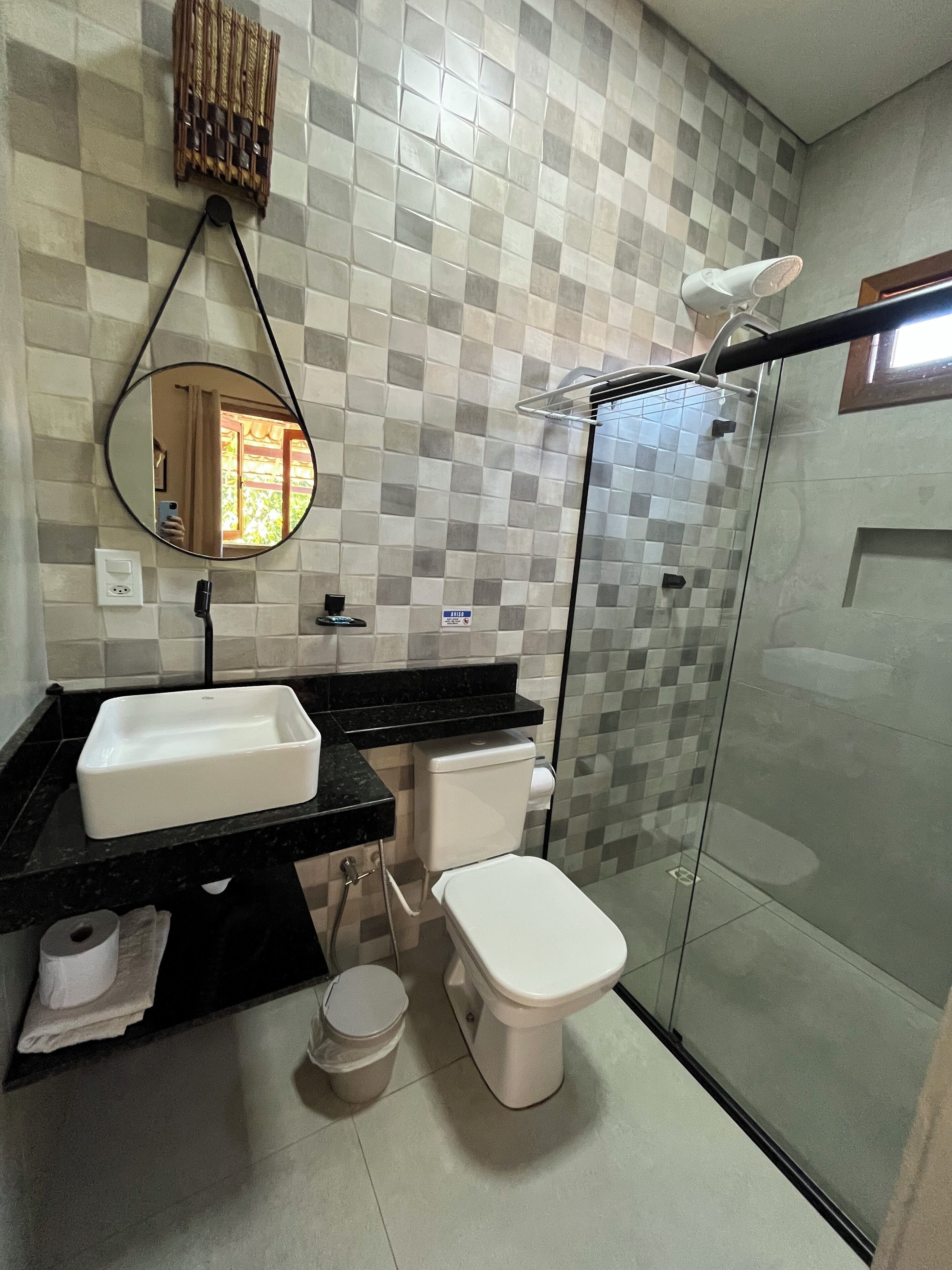 Un baño moderno con salpicadero de azulejos a cuadros, encimera negra, lavabo blanco, inodoro y cabina de ducha de vidrio.