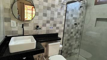 Un baño moderno con salpicadero de azulejos a cuadros, encimera negra, lavabo blanco, inodoro y cabina de ducha de vidrio.