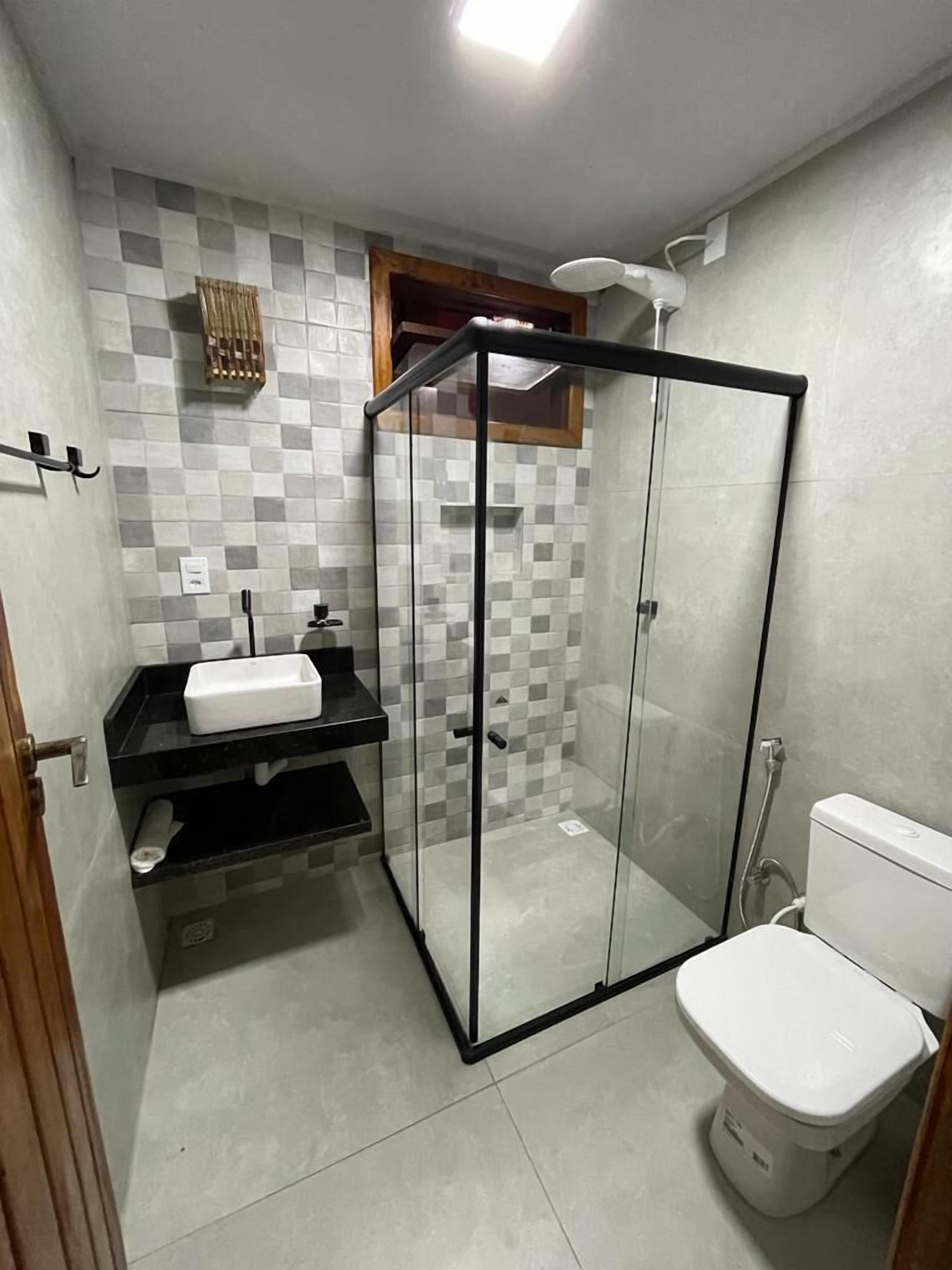 Une petite salle de bain dotée d’une douche à parois de verre, de toilettes blanches et d’un lavabo noir avec un miroir.