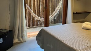A bedroom with a bed, a TV, a hammock, and a view of the outside. - Pousada Vilarejo (Itacaré)