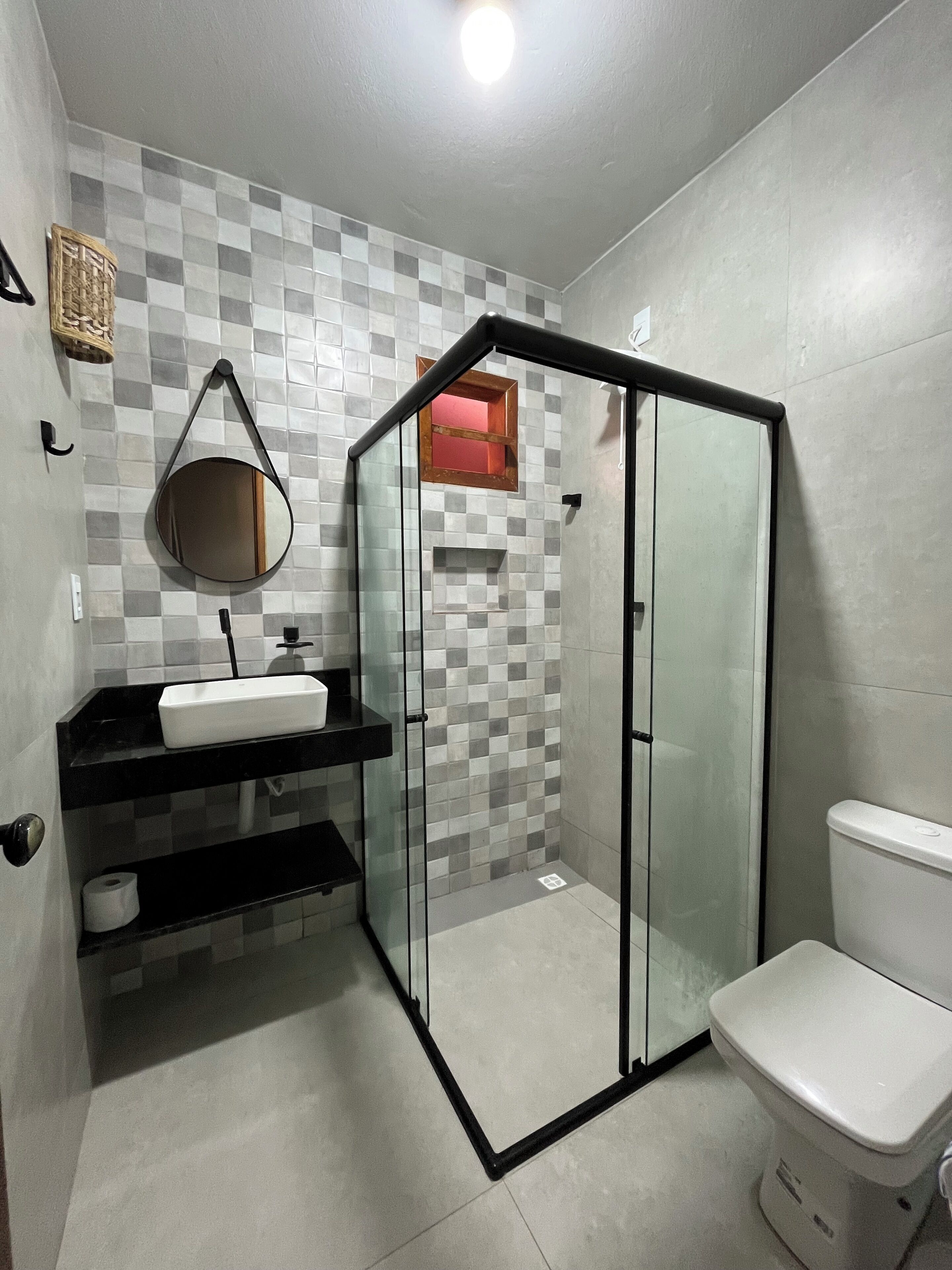 A modern bathroom with a glass shower enclosure, a white toilet, and a black vanity with a mirror.