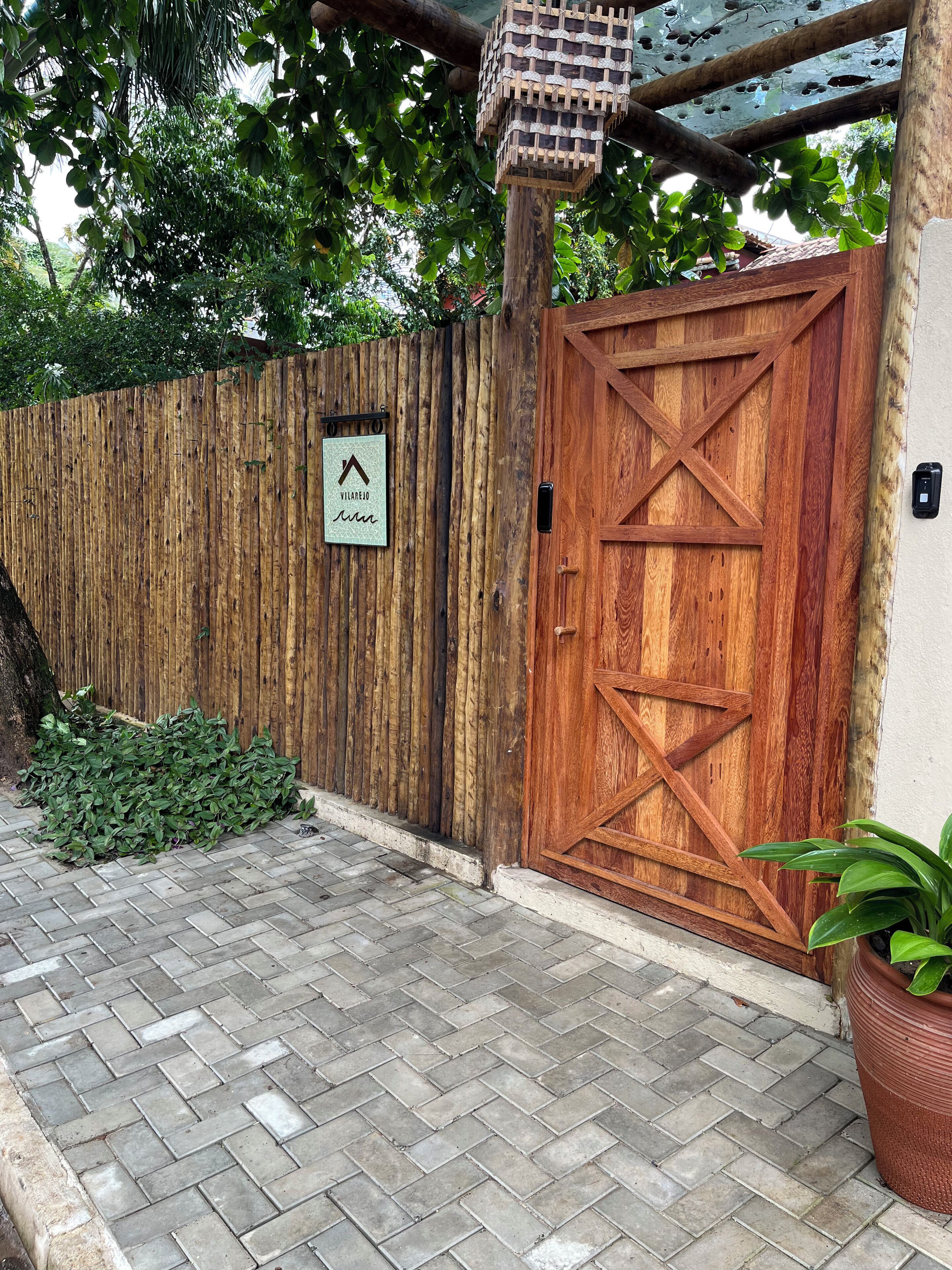 Una verja de madera con un cartel, un acceso adoquinado de ladrillo y una planta en maceta.
