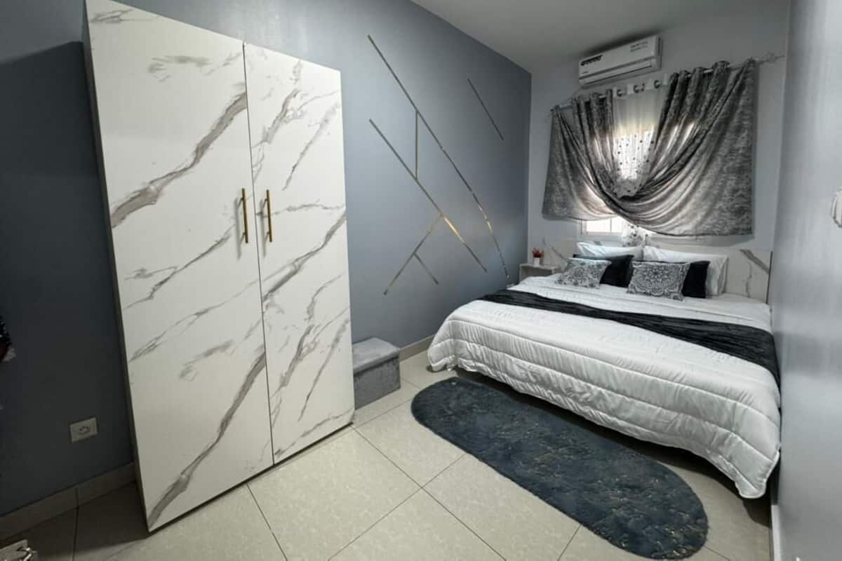 A bedroom with a bed, a wardrobe, a nightstand, and a window with curtains.