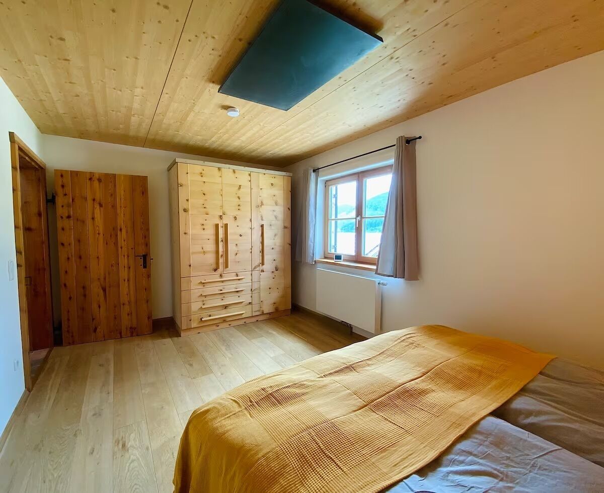 A room with a bed, wooden wardrobe, and a window with curtains.