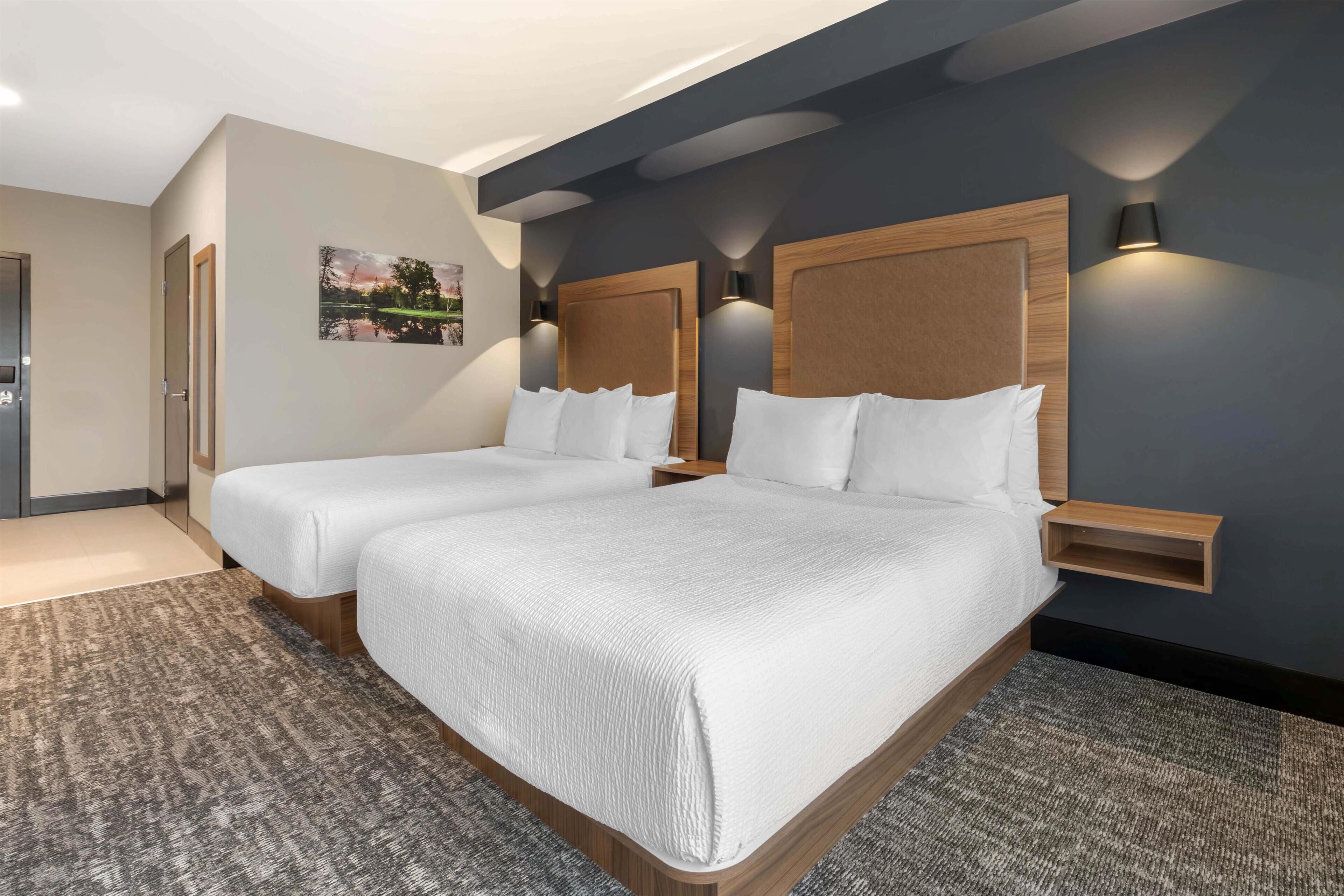 Une chambre d’hôtel avec un lit double, une petite table de chevet, une lampe fixée au mur et un tableau encadré accroché au mur.