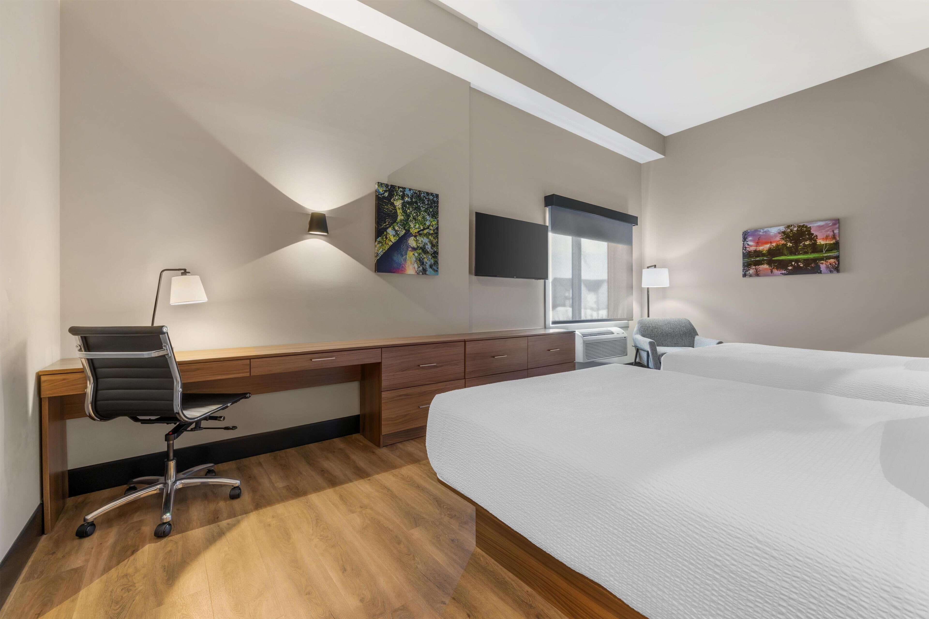 A hotel room with a large bed, a desk with a chair, a flat-screen TV, and artwork on the walls.