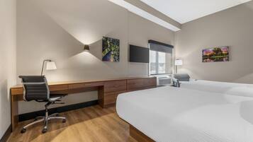 A hotel room with a large bed, a desk with a chair, a flat-screen TV, and artwork on the walls.