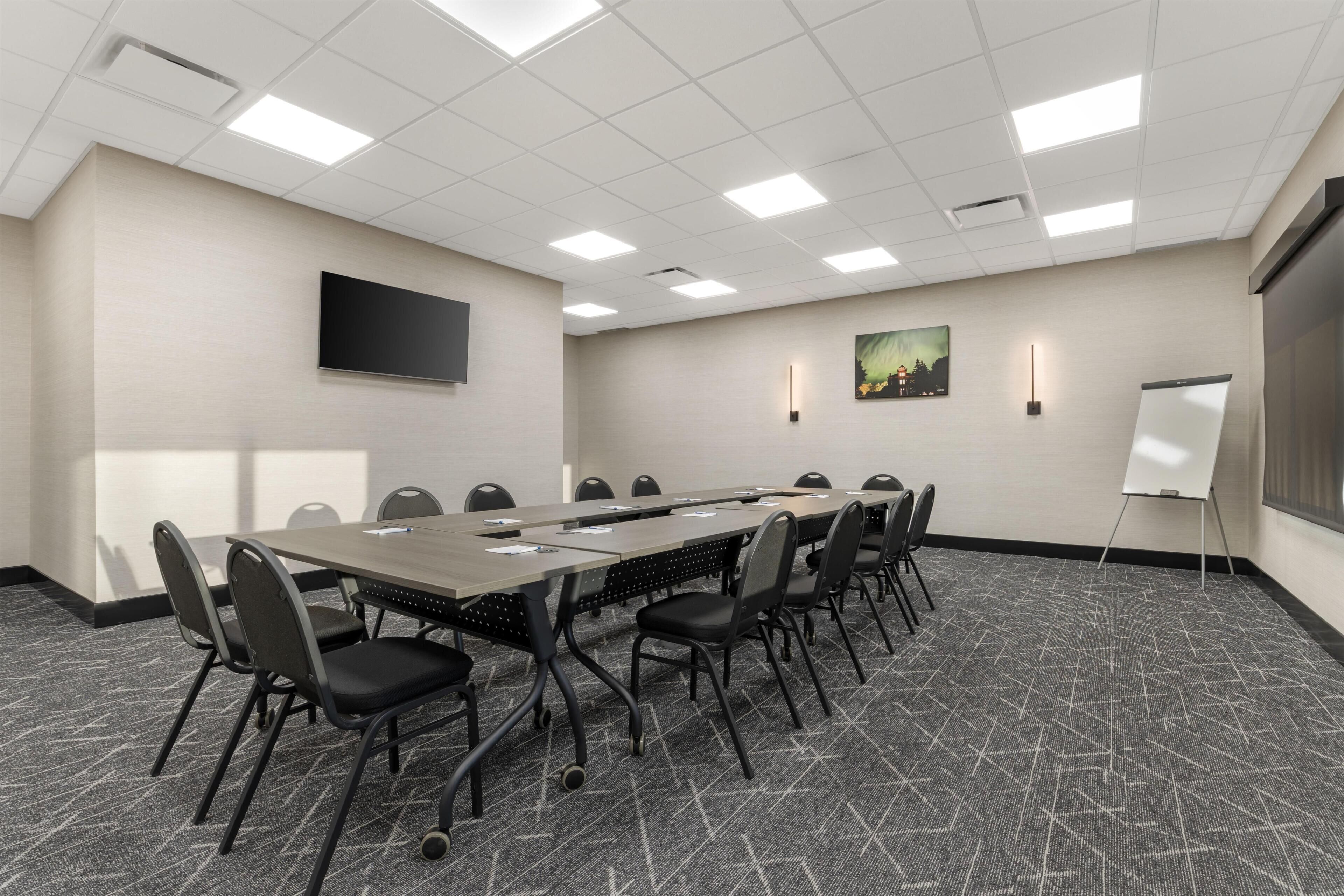 Une salle de conférence avec une longue table, des chaises, un téléviseur à écran plat, un tableau blanc et un tableau accroché au mur.