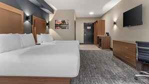 Quarto de hotel com uma cama grande, uma escrivaninha, uma televisão de tela plana e uma porta que dá para uma cozinha compacta.