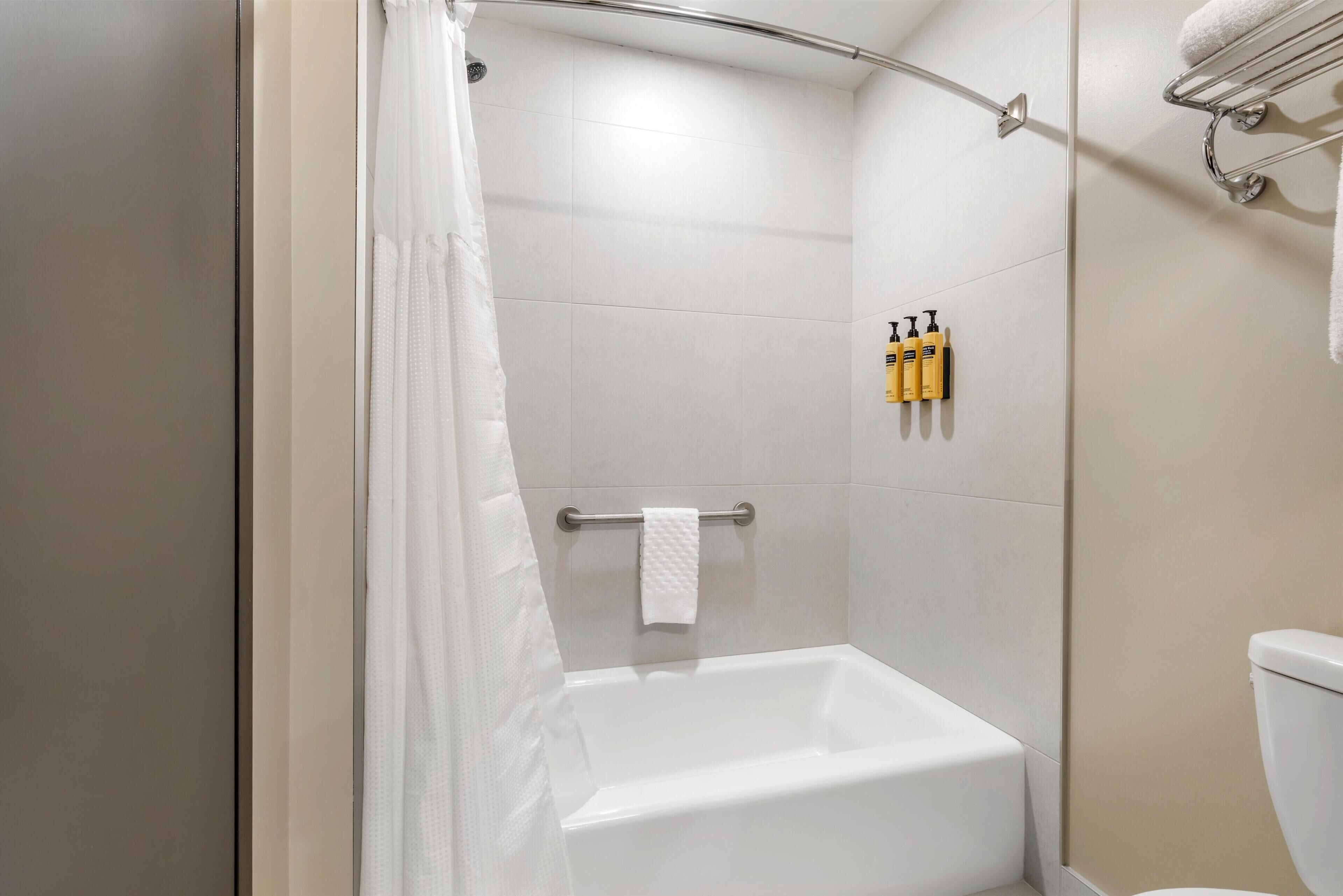 Une douche avec une porte en verre, une serviette blanche sur un porte-serviettes et des articles de toilette accrochés au mur.