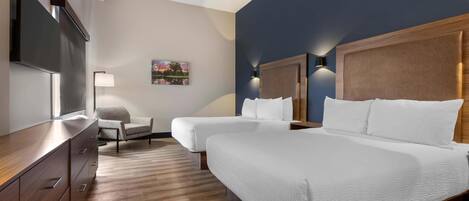 A hotel room with two beds, a desk, a chair, a TV, and a painting on the wall.