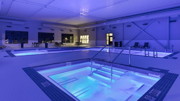 Uma grande piscina interior com várias pistas de natação, área de estar com cadeiras e um balcão de receção.