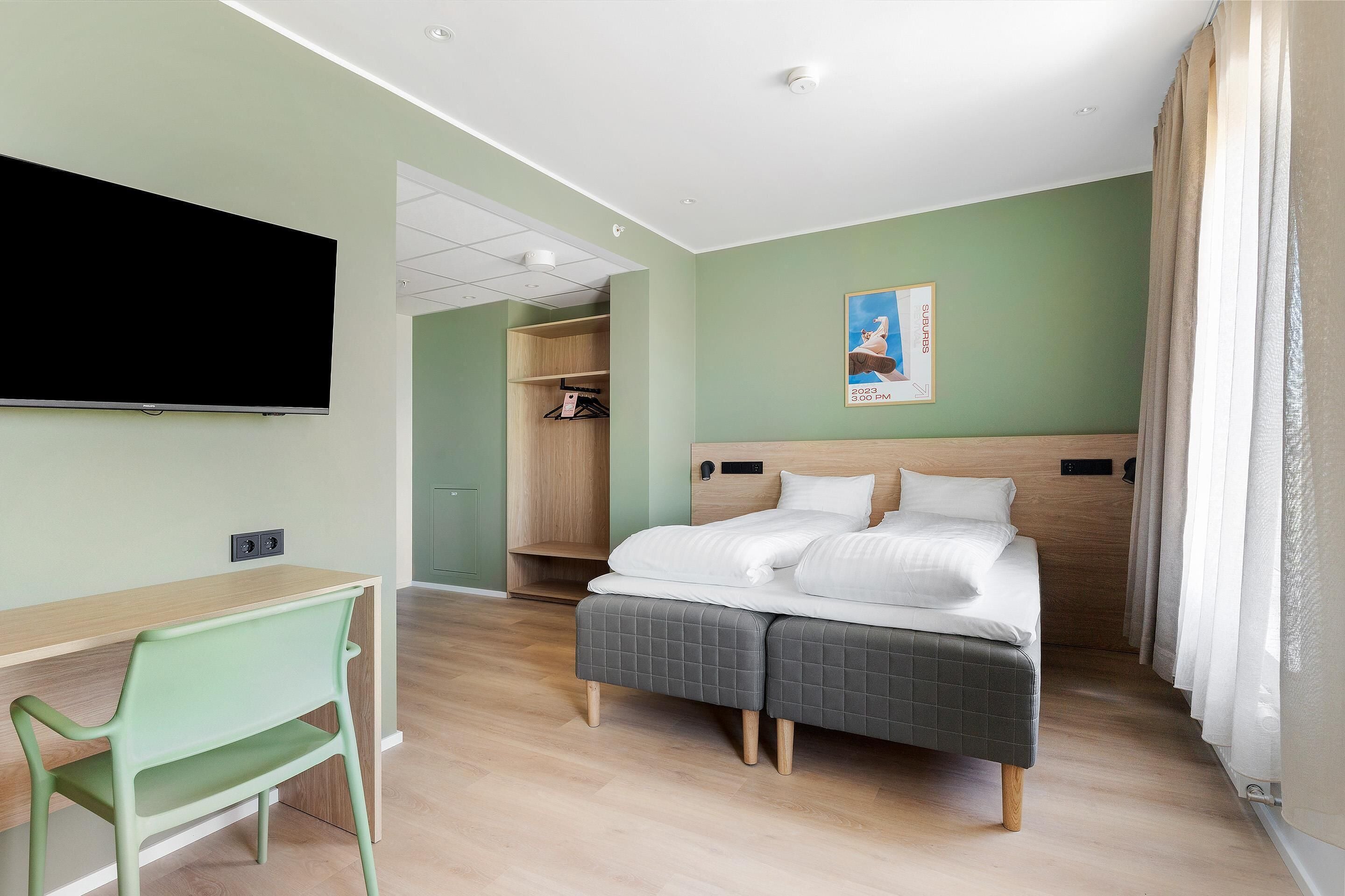 Ein Hotelzimmer mit Bett, Schreibtisch, Stuhl, Kleiderschrank und Fernseher.