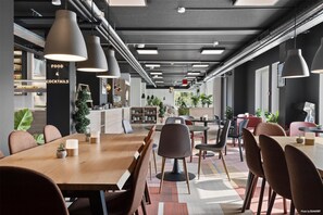 A modern dining area with a long wooden table, multiple chairs, pendant lighting, and a kitchen area in the background. - Aiden By Best Western Odense (Odense)