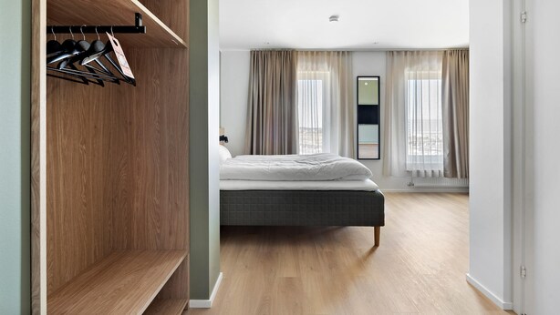 A bedroom with a bed, wooden wardrobe, and a view of the city through large windows. - Aiden By Best Western Odense (Odense)
