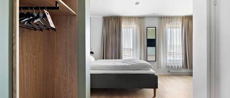 A bedroom with a bed, wooden wardrobe, and a view of the city through large windows.