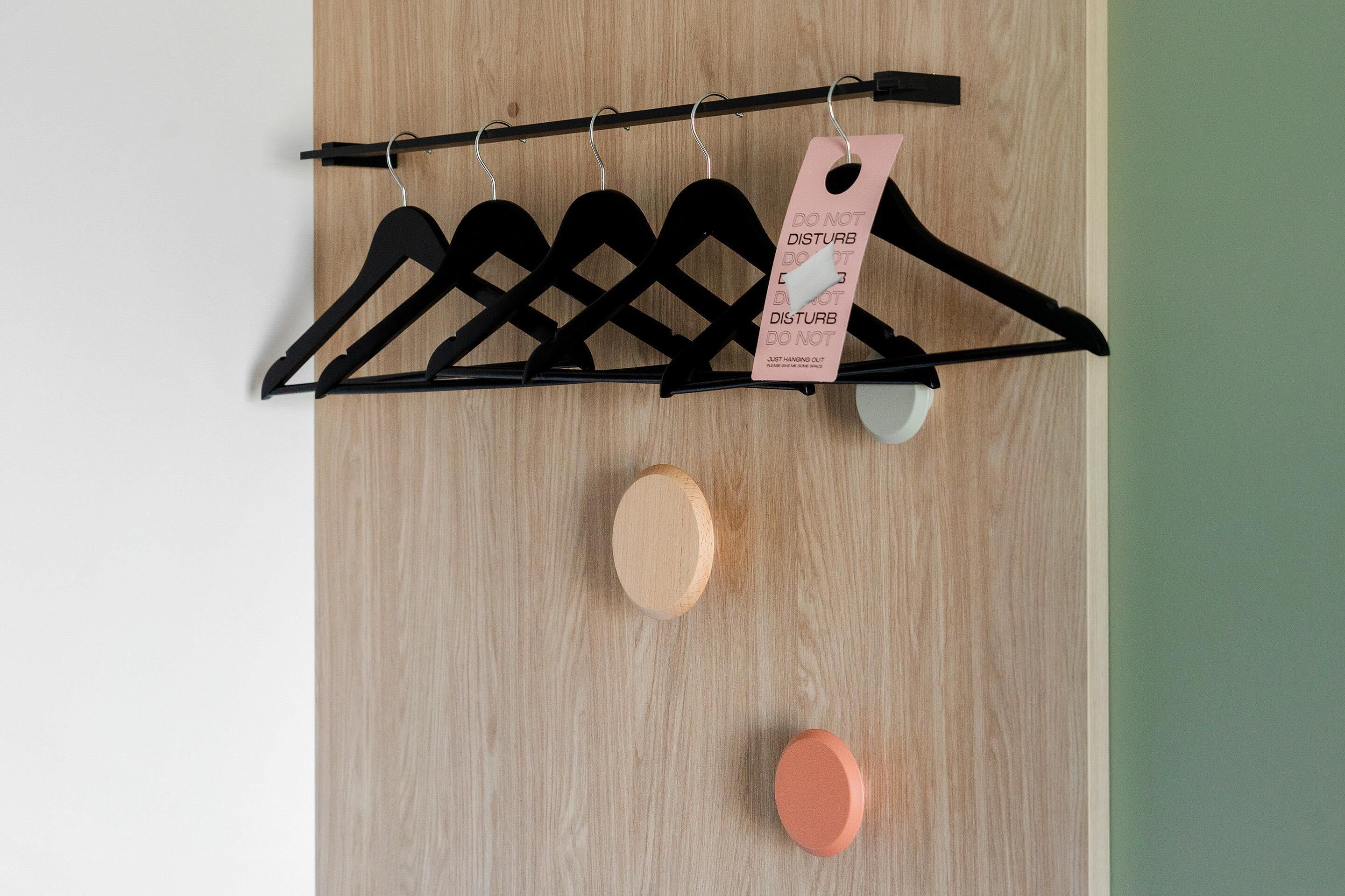 Eine Holzwand mit einem schwarzen Kleiderhaken, an dem mehrere schwarze Kleiderbügel und ein pinkfarbener Anhänger befestigt sind.