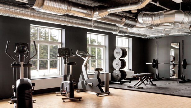 A gym with exercise equipment, large windows, and a mirror. - Aiden By Best Western Odense (Odense)