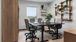 A modern meeting room with a large table, four chairs, and a wooden cabinet. There are shelves with plants on the wall and a window with a view of greenery. - Aiden By Best Western Odense (Odense)
